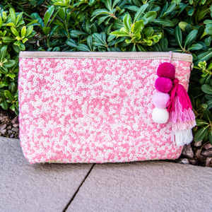 Straw clutch with pink sequins sitting against a green plant