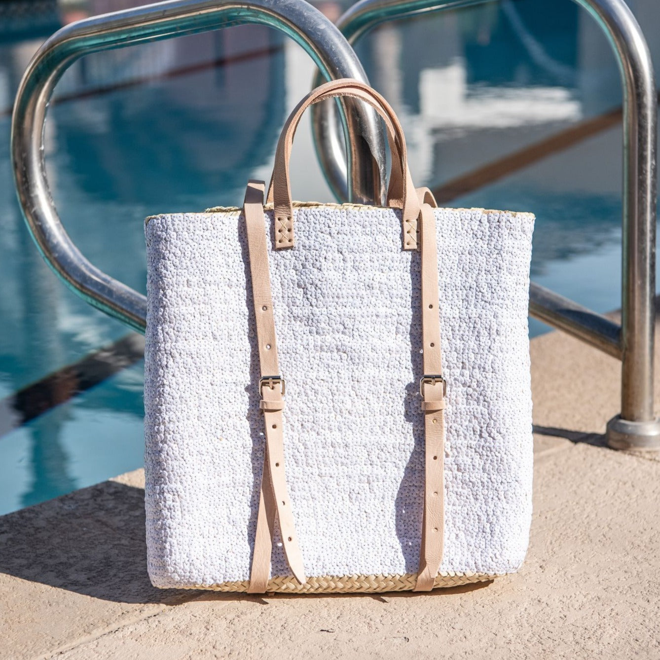 Straw backpack with white sequins sitting on pool deck