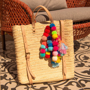 Handcrafted Straw Backpack with Pom Pom Tassels sitting against a chair