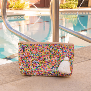 Straw clutch with multi-colored sequins sitting on pool deck