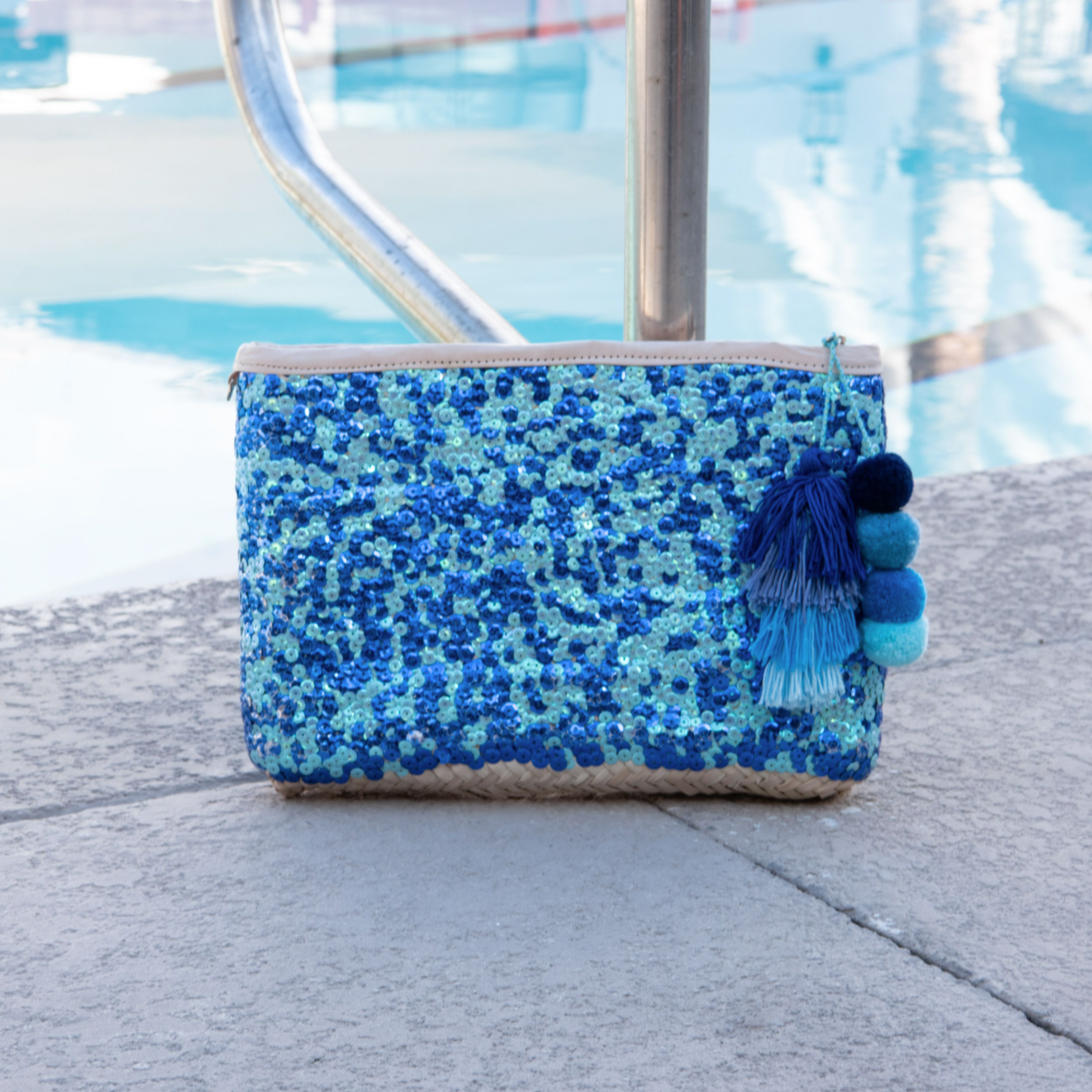 Straw clutch with blue sequins sitting next to a pool