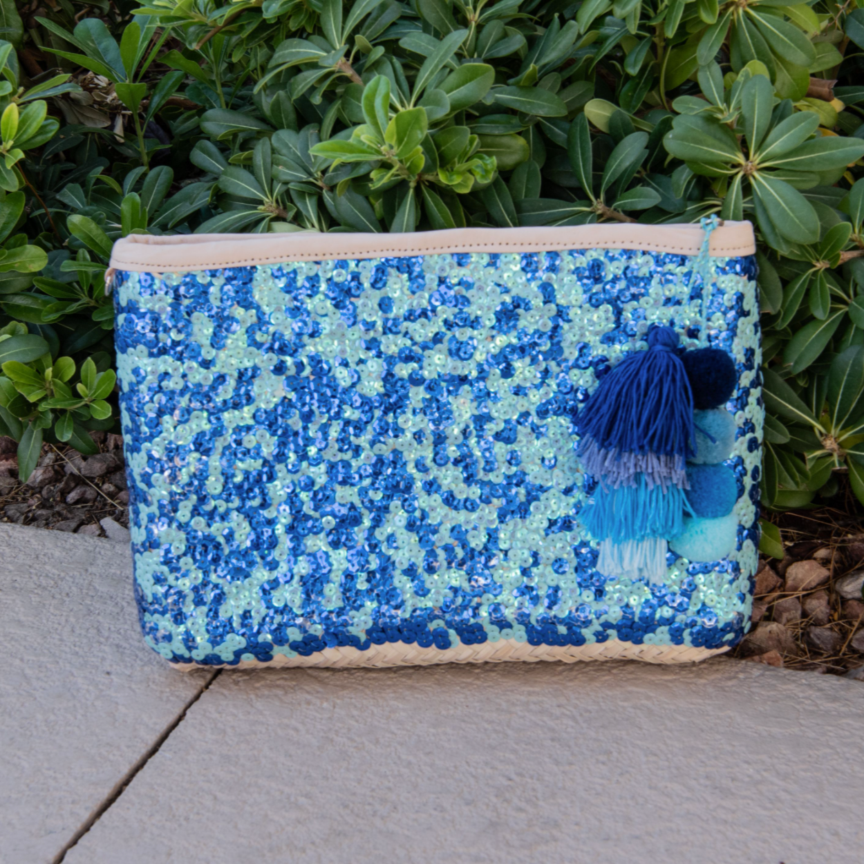 Straw clutch with blue sequin sitting against a green plant